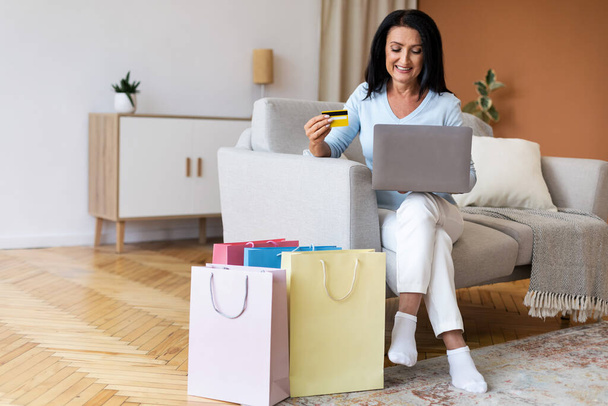 Kypsä nainen käyttää kannettavaa tietokonetta ja luottokorttia kotona - Valokuva, kuva