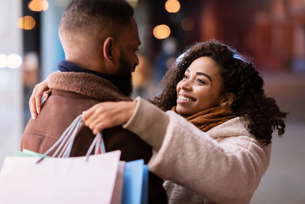 Feliz pareja negra abrazando y sosteniendo bolsas de compras - Foto, Imagen