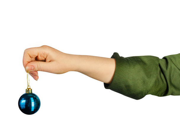 Foto aislada de una mano de niña en camisa verde que sostiene el juguete decorativo de la bola de Navidad sobre fondo blanco. - Foto, Imagen