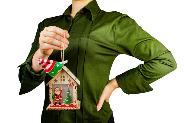 片手でクリスマスの木製のおもちゃの家の装飾を保持緑のシャツの女の子の孤立した写真. - 写真・画像