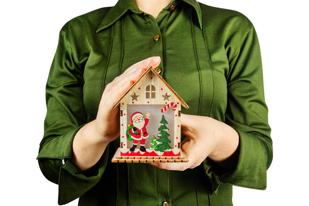 Foto isolada de uma menina de camisa verde segurando uma decoração de casa de brinquedo de madeira de Natal. - Foto, Imagem