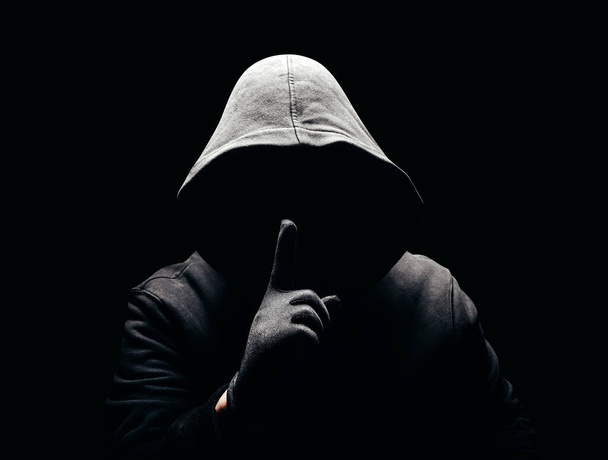 Photo of a scary horror man in hoodie showing silence hand sign in dark. - Foto, afbeelding