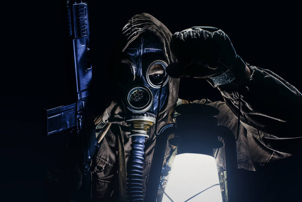 Guerriero stalker in maschera antigas sovietica protettiva con lanterna a benzina con arma su sfondo nero. - Foto, immagini