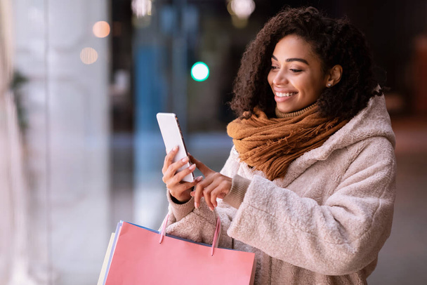 Felice donna nera utilizzando smartphone, tenendo borse della spesa - Foto, immagini
