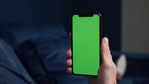 Close up shot of guy lying on couch at night, holding a smartphone with chroma key mock up green screen - technology, connections, communications concept 4k video template - Video