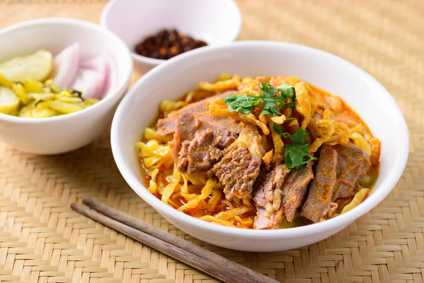 Comida tailandesa del norte (Khao Soi), sopa de fideos al curry picante con carne de res comiendo con mostaza en escabeche, chalota, lima y chile molido frito en aceite - Foto, Imagen