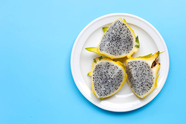 Żółty pitahaya lub smoczy owoc na białym talerzu na niebieskim tle. Przestrzeń kopiowania - Zdjęcie, obraz