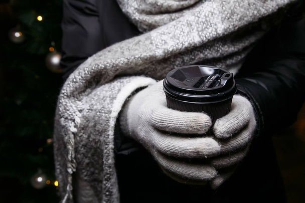 manos en manoplas sostienen una taza de café caliente. Café para llevar en invierno - Foto, imagen