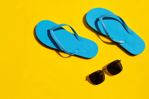 Sarı arka planda güneş gözlüklü mavi terlikler. Yaz tatili kavramının tadını çıkar. - Fotoğraf, Görsel