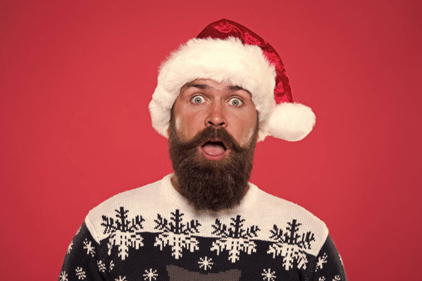 new year party. Unexpected surprise. surprised bearded man santa hat. brutal hipster favorite sweater red background. winter holiday fun. surprised face mustache. portrait of santa man with beard - Photo, Image