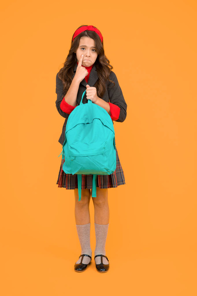 Unhappy crying little kid hold school bag wearing formal uniform yellow background, back to school - Фото, изображение