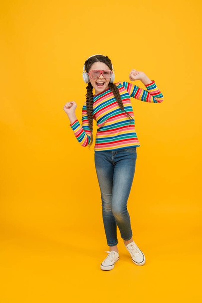 happy teen girl wear modern headphones. funny kid listen music. beauty in glamour glasses. childhood happiness. smiling child on yellow background. hipster party fashion style. Spreading knowledg - Foto, Bild