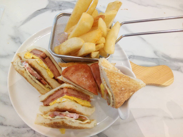 Home made the club or clubhouse sandwich with fries.Layers of ham, bacon and turkey with juicy tomatoes, crisp lettuce and cheddar cheese create the perfect bite! Club sandwich reveal what's in it. Club stands for "chicken and lettuce under bacon" - Photo, Image