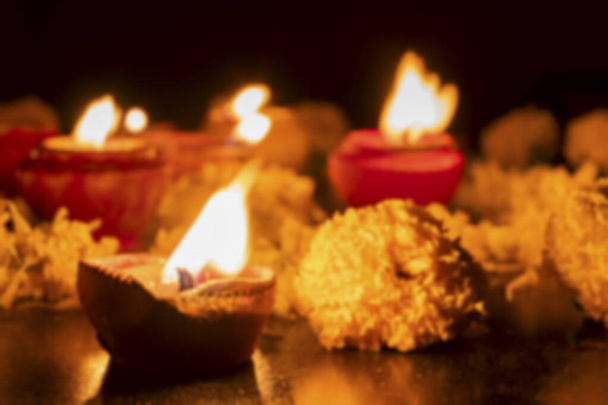 Unscharfes Bild von sehr niedrigen Blickwinkel von Rangoli Blumen und Kerzen oder Diyas, Deepawali Lichter in der Nacht. Dunkler Hintergrund. - Foto, Bild