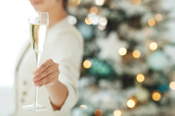 Donna sorridente con bicchiere di spumante sotto le luci dell'albero di Natale sfondo. - Foto, immagini