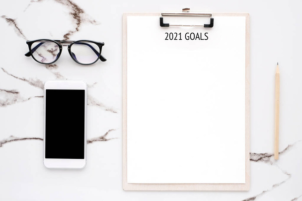 2021 goals on blank note paper with copy space for text and smartphone with blank screen on white marble background, new year aim to success in business background - Photo, Image