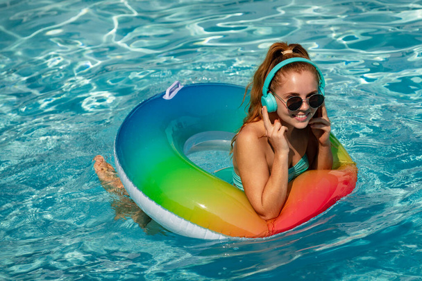 Літня музика. Чудова молода жінка позує в бікіні біля басейну, слухає музику. Літні канікули. Насолоджуючись жінкою в бікіні в басейні з навушниками
. - Фото, зображення