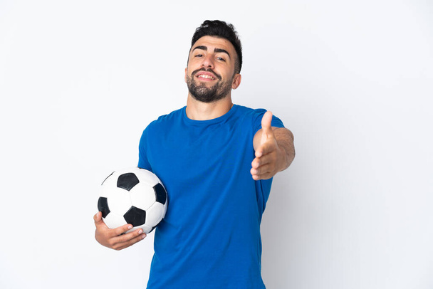 Guapo joven jugador de fútbol hombre sobre pared aislada estrechando las manos para cerrar una buena oferta - Foto, imagen