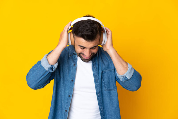 Caucasian man over isolated yellow background listening music - Zdjęcie, obraz