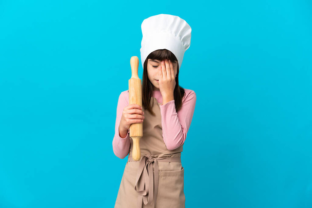 Little girl holding a rolling pin isolated on blue background with tired and sick expression - 写真・画像