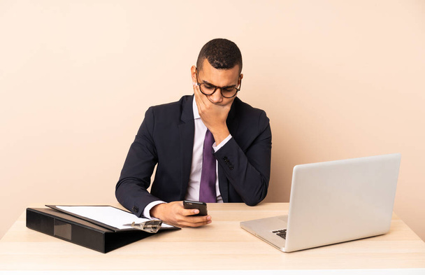 Young business man in his office with a laptop and other documents thinking and sending a message - Foto, Imagen