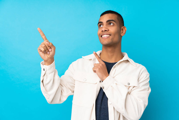 Молодий афроамериканець через ізольований синій фон вказує з вказівним пальцем чудова ідея - Фото, зображення