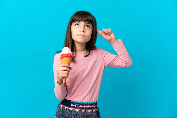 Petite fille avec une crème glacée cornet isolé sur fond bleu ayant des doutes et la pensée - Photo, image