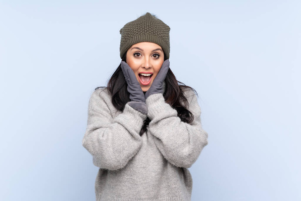 Young Colombian girl with winter hat over isolated blue background with surprise facial expression - Foto, immagini