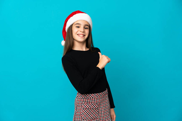 Маленька дівчинка з різдвяним капелюхом ізольована на синьому фоні горда і самовдоволена
 - Фото, зображення