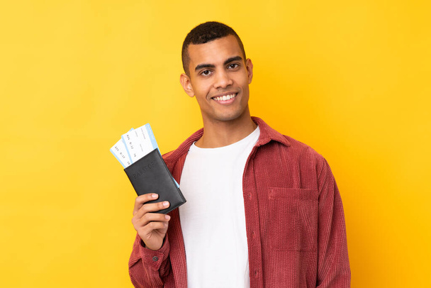 Junger Afroamerikaner mit gelbem Hintergrund glücklich im Urlaub mit Pass und Flugtickets - Foto, Bild