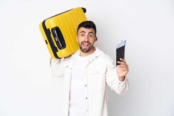Кавказский мужчина на изолированном белом фоне в отпуске с чемоданом и паспортом - Фото, изображение
