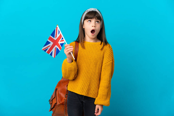 Kislány tanul angol elszigetelt kék háttér felnéz, és meglepett arckifejezéssel - Fotó, kép
