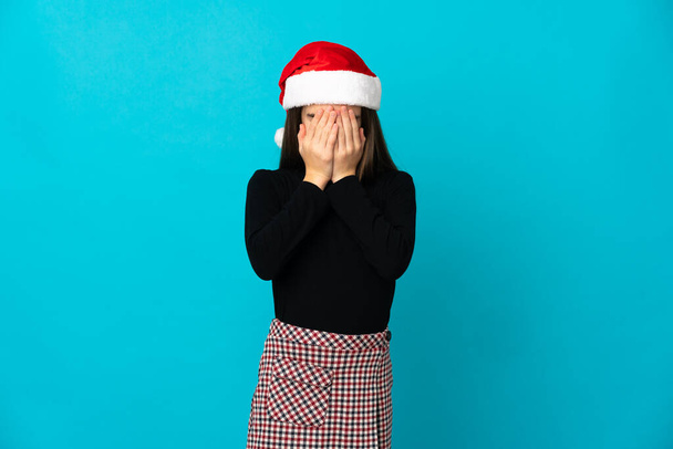 Niña con sombrero de Navidad aislado sobre fondo azul con expresión cansada y enferma - Foto, imagen
