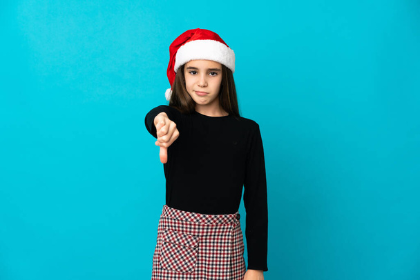 Little girl with Christmas hat isolated on blue background showing thumb down with negative expression - Foto, Imagem