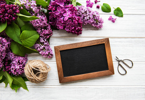 Fresh lilac flowers frame over wooden background with copy space on blackboard, flat lay floral composition - Фото, изображение