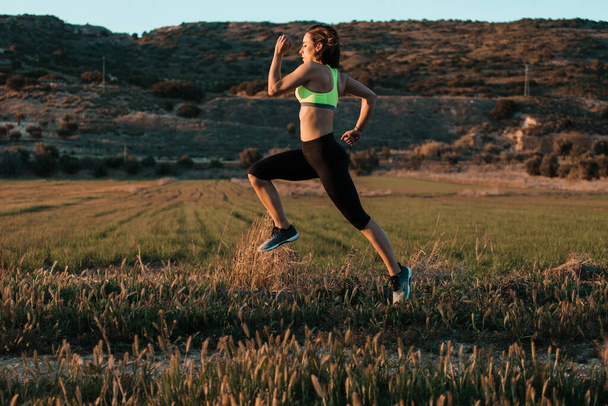 Woman runner running through the spring meadow. Workout in a nature. - Photo, Image