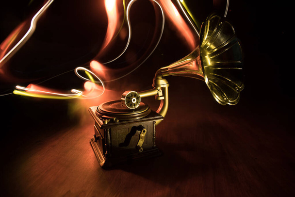 Musikkonzept. Altes Grammophon auf dunklem Hintergrund. Retro-Grammophon mit Scheibe auf Holztisch mit getönter Hintergrundbeleuchtung. Selektiver Fokus - Foto, Bild