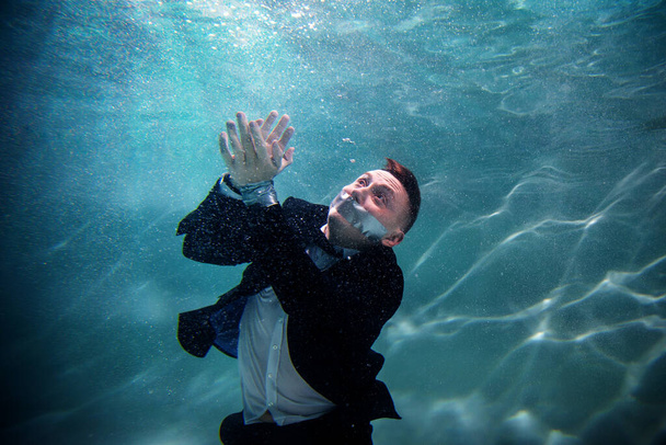 Cute beginner young businessman with his mouth taped and hands tied underwater. Drowning competitors in pond. Concept successful business and achieving your goal among competitors. Copy space - Foto, Imagem