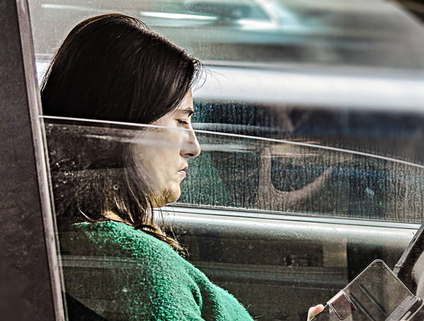 Profilo di donna che guarda il cellulare in auto su uno sfondo sfocato - Foto, immagini