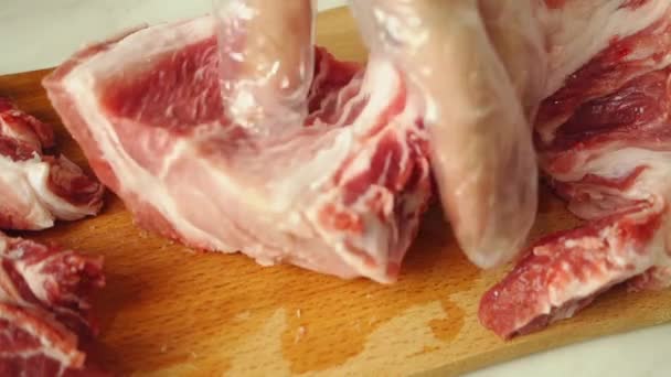 Un uomo con i guanti taglia la carne a strati. Un pezzo di carne succoso e grasso viene tagliato con un coltello su una tavola di legno. - Filmati, video