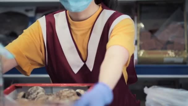 Een vrouwelijke werknemer in uniform, met rubberen handschoenen, en een medisch masker, verpakt peperkoek in een wegwerp plastic zak. Handen van dichtbij. - Video