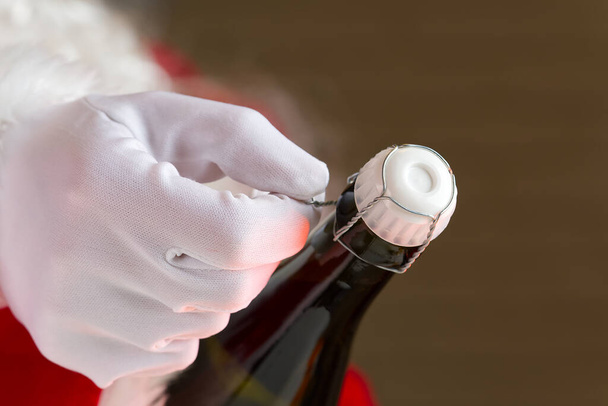 Человек в костюме Санта Клауса открывает бутылку шампанского - Фото, изображение
