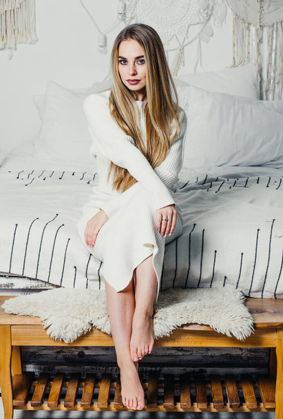 junge Frau mit langen luxuriösen blonden Haaren auf dem Bett im Schlafzimmer in weißen Tönen Interieur - Foto, Bild