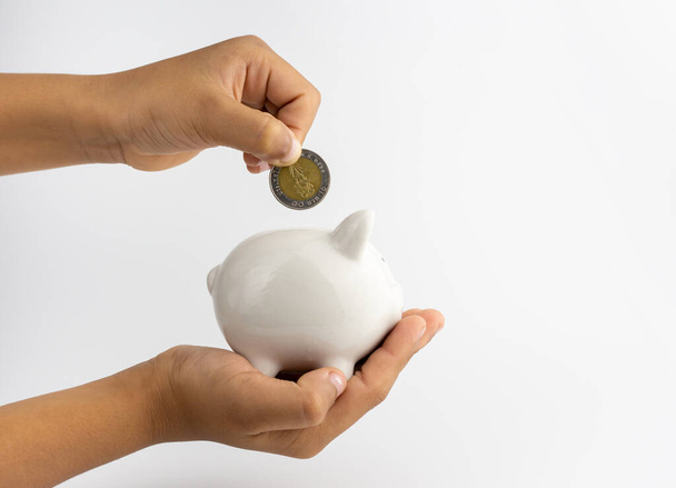 A piggy bank in hand and is putting coins in a piggy bank with copy space on white background. - Foto, immagini