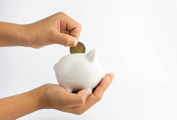 A piggy bank in hand and is putting coins in a piggy bank with copy space on white background. - Photo, Image