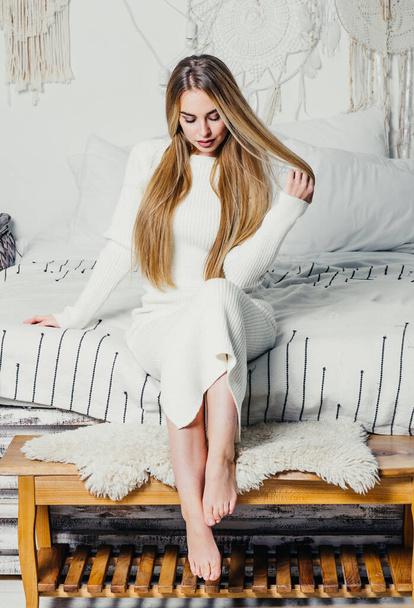 jeune femme avec de longs cheveux blonds blonds de luxe sur le lit dans la chambre à coucher dans des tons blancs intérieur - Photo, image