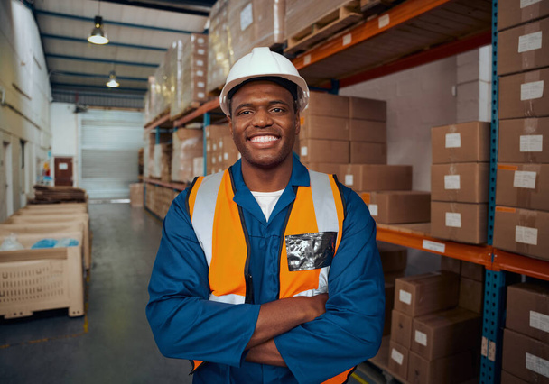 Portrait of a confident african factory engineer standing with his arm crossed in large warehouse - Fotografie, Obrázek