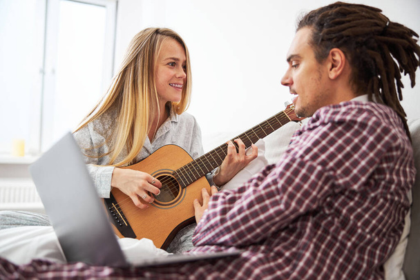 Happy young woman playing guitar and spending time with boyfriend - Foto, Bild