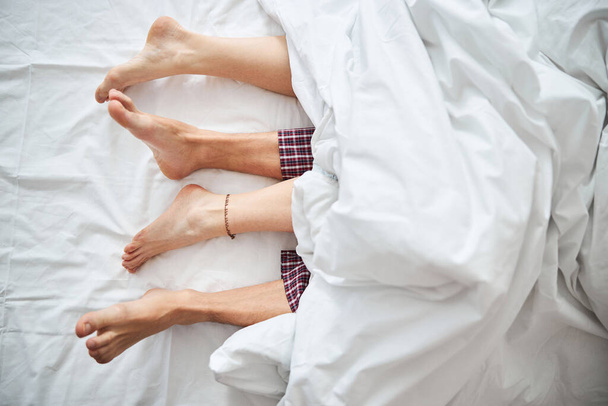 Çıplak ayakla yatakta uzanan sevgi dolu genç bir çift - Fotoğraf, Görsel