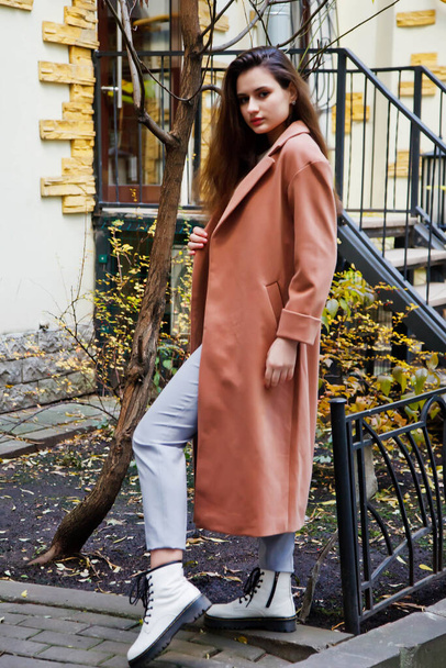 Fashionable young beautiful stylish woman in brown coat walking on street. Autumn fashion trend for smiling, happy, purposeful female. Concept style, fashion, beauty and achievement goals. Copy space - Fotó, kép